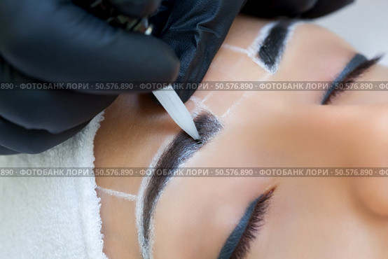 Permanent make-up for eyebrows of beautiful woman with thick brows in beauty salon. Closeup beautician doing  tattooing eyebrow. Стоковое фото, агентство Ingram Publishing / Фотобанк Лори