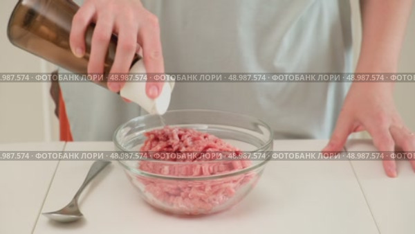Person adds salt to raw ground meat in a glass bowl, preparing ingredients for cooking or meal preparation on a kitchen counter. Стоковое видео, видеограф Андрей Журавлев / Фотобанк Лори
