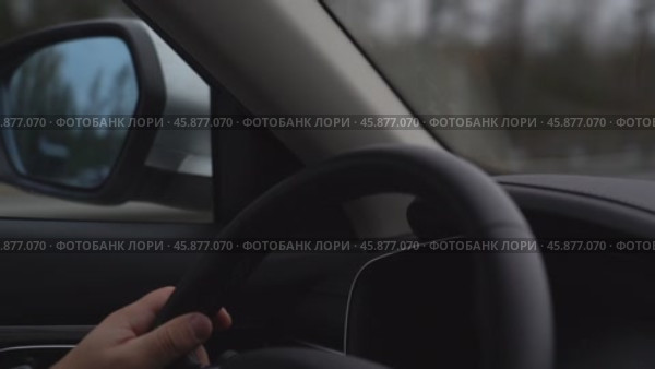 Person is driving a car and is holding the steering wheel. The car is on a road and there is a mirror on the side of the car. Стоковое видео, видеограф Скрипачев Антон / Фотобанк Лори