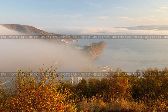 Петропавловск-Камчатский, Камчатский край, Россия. Красивый вечерний городской пейзаж. Вид сверху с Мишенной сопки на побережье Авачинской бухты и Никольскую сопку. Низкая облачность и туман скрывают историческую часть города. Вечернее золотистое освещение на закате. Путешествие на Камчатку. Дальний Восток России. Стоковое фото, фотограф Андрей Степанов / Фотобанк Лори