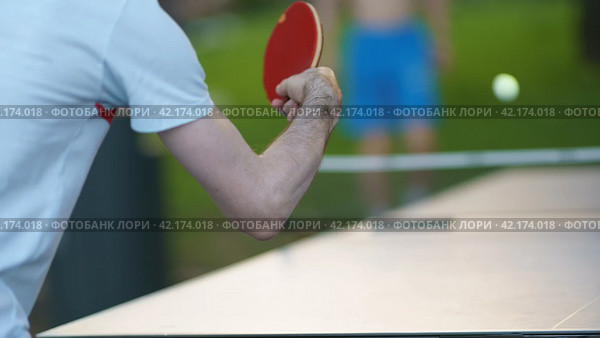 Photography of small racket, ball for table tennis in a player's hand on city street in spring day. It's laminated wooden bat covered with rubber on two sides. Play is fast, demands quick reactions. Стоковое фото, фотограф YuryKara / Фотобанк Лори