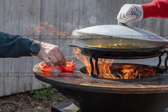 Picnic. Hands of a man cooking outdoors with friends using black hybrid grill and backyard. Man frying potatoes in a cauldron. Стоковое фото, фотограф Оксана Медведева / Фотобанк Лори