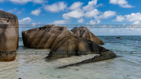 Picturesque granite boulders with smoothed folded slopes near the ocean shore. Turquoise water and blue sky with clouds. Seychelles. La Digue. Anse Source D’Argent beach. Стоковое фото, фотограф Вера Ивановна Кубарева / Фотобанк Лори