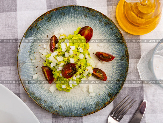 Pile of guacamole on plate, sprinkled with chopped hot onions, decorated with slices of tomatoes. Стоковое фото, фотограф Яков Филимонов / Фотобанк Лори