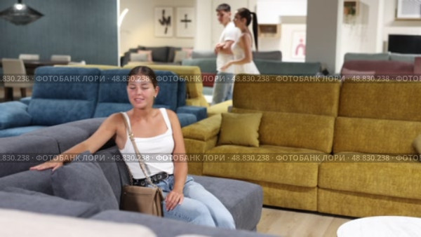 Pleased young girl choosing convenient sofa in large furniture shop. Стоковое видео, видеограф Яков Филимонов / Фотобанк Лори