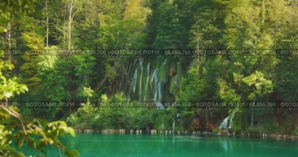Plitvice waterfall cascades down mossy rocks into blue lake in Croatia during summertime visit. Стоковое видео, видеограф Igor Tichonow / Фотобанк Лори