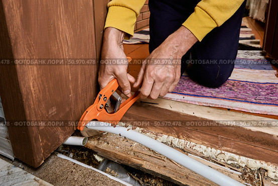 Plumber uses pipe cutter to remove leaking section from plastic tubing during replacement process at area where visible damage occurred earlier. Стоковое фото, фотограф Владимир Григорьев / Фотобанк Лори