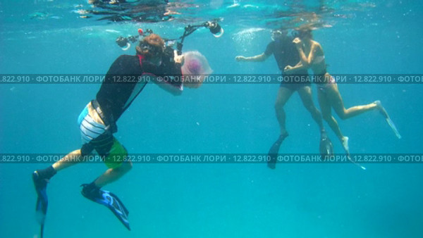 Подводный фотограф фотографирует под водой молодую пару на фоне медузы Цветная капуста (Cephea cephea), Индийский океан, Мальдивские острова (2015 год). Редакционное видео, видеограф Некрасов Андрей / Фотобанк Лори