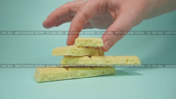 Полная рука берёт кусочек белого пористого шоколада. Кусочки белого шоколада пирамидкой на голубом фоне. Стоковое видео, видеограф Анна Чижова / Фотобанк Лори