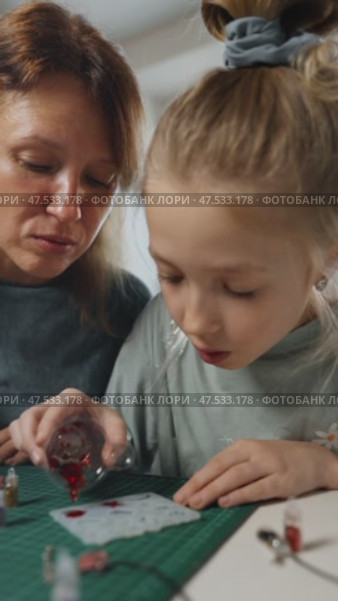 Popular trend epoxy resin jewelry making at home. Mom and girl enthusiastically pour epoxy resin mixed with red glitter into tiny mold to make jewelry, bringing their creative vision to life. Стоковое видео, видеограф Енваев Андрей / Фотобанк Лори