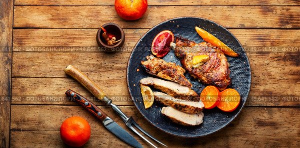 Pork on the bone baked in oranges, lime and tangerine. Meat in the plate on wooden table. Barbecue meat steak with citrus fruits. Стоковое фото, агентство Ingram Publishing / Фотобанк Лори