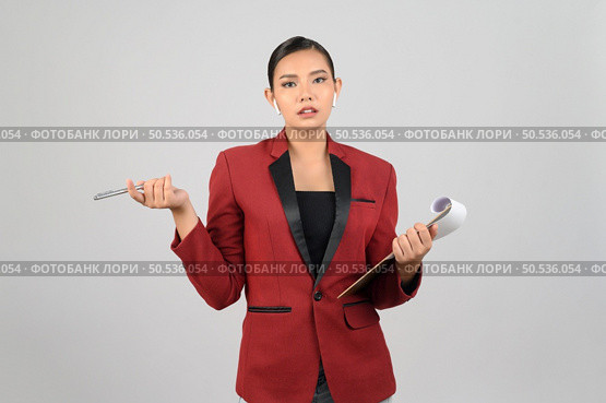 Portrait Asian young woman in officer uniform standing posture talking with wireless earphone and hold report paper on clipboard in hand,  isolated on white background. Стоковое фото, агентство Ingram Publishing / Фотобанк Лори