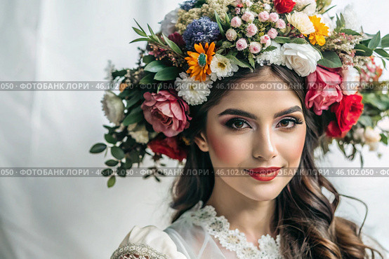 Portrait of a beautiful young woman in close-up with a floral tiara or a wreath on her head on a white background. Spanish culture, Latin American heritage. Стоковое AI-изображение, AI-художник Photojuli / Фотобанк Лори