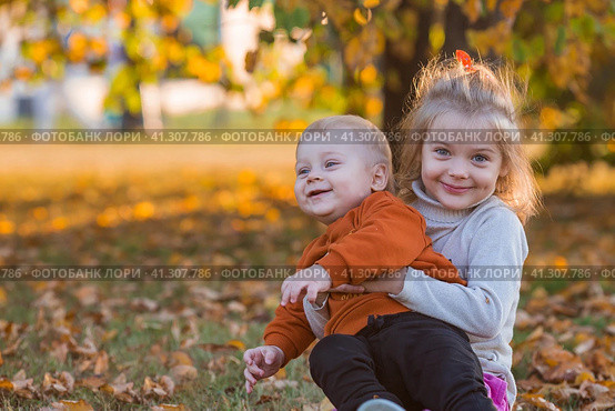 Portrait of a little boy 9 months old and a girl 4 years old outdoors. Happy children are playing in the autumn park. Sister hugs brother. Happy childhood and motherhood. Стоковое фото, фотограф Photojuli / Фотобанк Лори