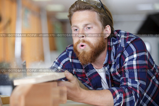 portrait of focused modern carpenter blowing sawdust off workstation. Стоковое фото, агентство Ingram Publishing / Фотобанк Лори
