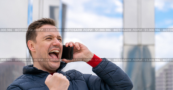 Portrait of handsome millennial man who received amazing news on phone, looking forward, clenching his fist in winners gesture and screaming yeah. Стоковое фото, фотограф Данила Большаков / Фотобанк Лори
