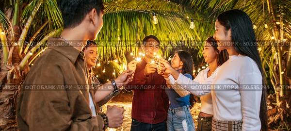 Portrait of Happy Asian group of friends having fun with sparklers outdoor - Young people having fun with fireworks at night time  - People, food, drink lifestyle, new year celebration concept. Стоковое фото, агентство Ingram Publishing / Фотобанк Лори