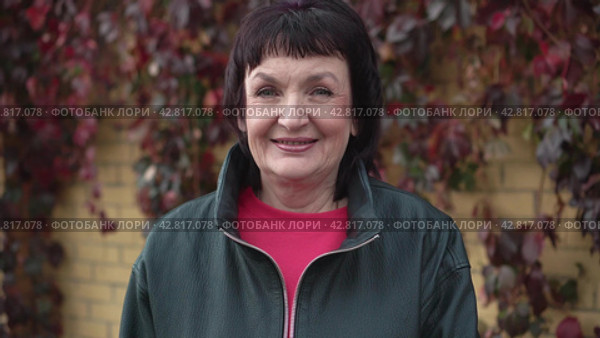 Portrait of happy mature woman buttoning zipper on gray leather jacket smiling outdoors. Стоковое видео, видеограф EStarodubov / Фотобанк Лори
