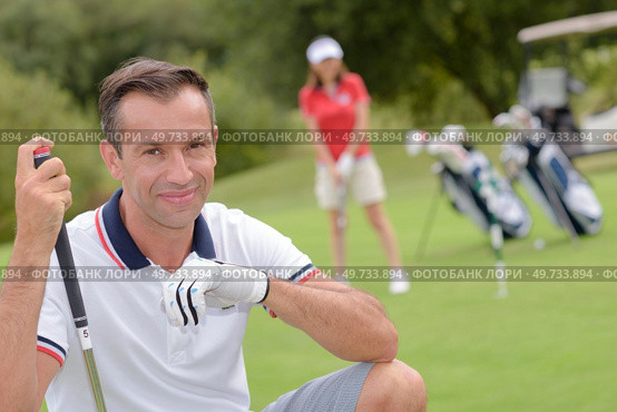 Portrait of male golfer, wife playing in background. Стоковое фото, агентство Ingram Publishing / Фотобанк Лори