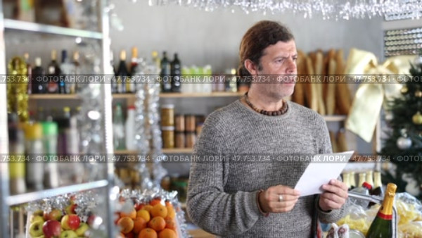 Portrait of modern man with cart shopping at supermarket, looking for something and reviewing and checking list of products to buy. Christmas shopping. Стоковое видео, видеограф Яков Филимонов / Фотобанк Лори