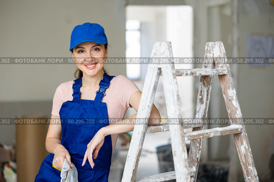 Portrait of positive builder woman in blue overalls next to stepladder. Стоковое фото, фотограф Яков Филимонов / Фотобанк Лори