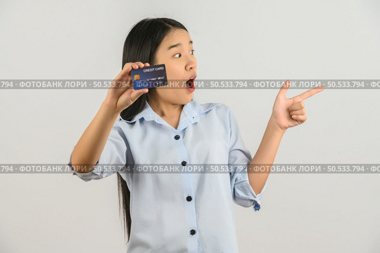 Portrait of positive young asian woman showing credit card good mood salary and pointing finger at aside isolated on white background. Finance, currency, payment and people concept. Стоковое фото, агентство Ingram Publishing / Фотобанк Лори