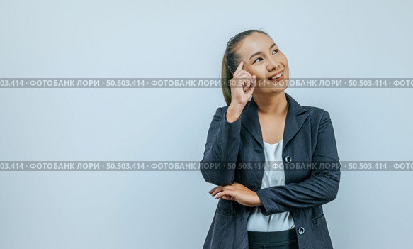 Portrait of smiling Asian woman wearing casual clothes pointing to head with one finger and looking away at empty space aside, isolated over background in studio. Стоковое фото, агентство Ingram Publishing / Фотобанк Лори