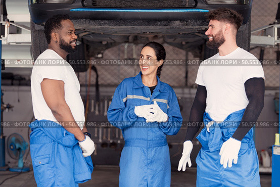 Portrait of smiling team of mechanics in auto repair shop,  Talking one another while standing under car. Стоковое фото, агентство Ingram Publishing / Фотобанк Лори