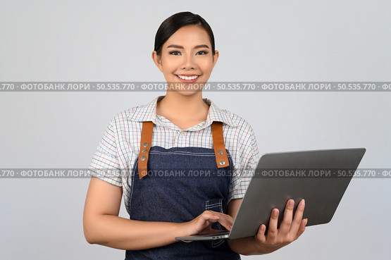 Portrait of young asian woman in waitress uniform holding a laptop computer posture, copy space to insert products for advertisement isolated on white background. Стоковое фото, агентство Ingram Publishing / Фотобанк Лори