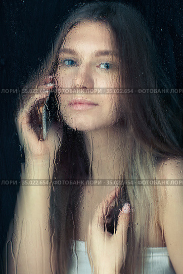 Portrait of young blonde woman with phone hands behind the window glass with raindrops. Стоковое фото, фотограф Сергей Пристяжнюк (Serg Zastavkin) / Фотобанк Лори