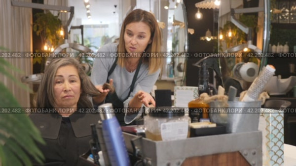 Portrait of young woman professional hair stylist talking to elderly female client in salon, choosing new hairdo. Стоковое видео, видеограф Яков Филимонов / Фотобанк Лори