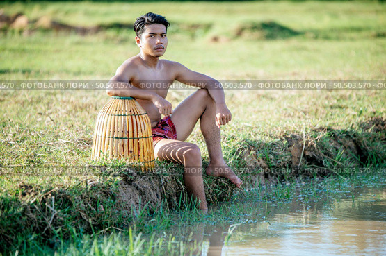 Portrait Young man topless use bamboo fishing trap to catch fish for cooking, Asian young farmer man in rural lifestyle, blurred buffalo is soaking in the swamp. in background. Стоковое фото, агентство Ingram Publishing / Фотобанк Лори