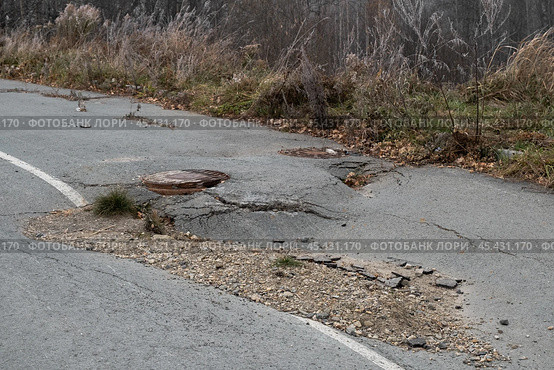 Pothole damage on a rural road surrounded by trees in autumn highlights urgent need for repairs. Стоковое фото, фотограф Георгий Мякишев / Фотобанк Лори