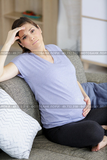 pregnant woman has stomachache sitting on her couch. Стоковое фото, агентство Ingram Publishing / Фотобанк Лори
