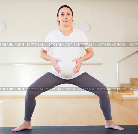 Pregnant woman is engaged in yoga. A pregnant woman practices yoga in the hall. Goddess Pose or utkata konasana. Стоковое фото, фотограф Татьяна Яцевич / Фотобанк Лори