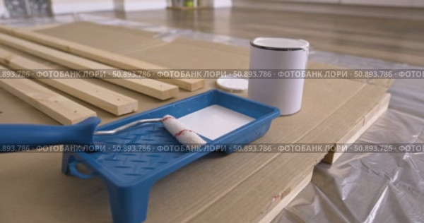 Preparation of paint roller for painting wooden planks, dipping roller in white paint tray. Pouring paint from can into tray close-up of tools, wood board protective film cardboard, renovation process. Стоковое видео, видеограф Сергей Тимофеев / Фотобанк Лори