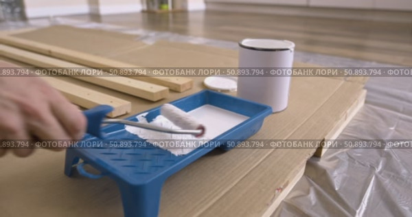 Preparation of paint roller for painting wooden planks, dipping roller in white paint tray. Pouring paint from can into tray close-up of tools, wood board protective film cardboard, renovation process. Стоковое видео, видеограф Сергей Тимофеев / Фотобанк Лори