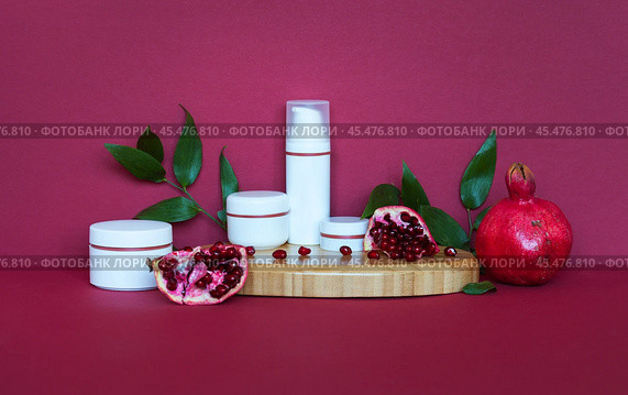 Presentation of natural cosmetics: anti-aging face creams, eyelids and moisturizing gel with extract of pomegranate on wooden podium and burgundy background. Using vitamin fruit extracts for cosmetics. Стоковое фото, фотограф Виктория Катьянова / Фотобанк Лори