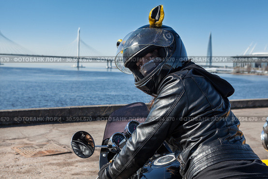 Pretty biker girl in leather jacket and black helmet with mask on face looking back while sitting in motorcycle. Стоковое фото, фотограф Кекяляйнен Андрей / Фотобанк Лори