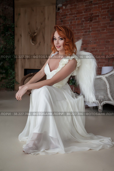 Pretty, slender woman with wings. Female in stage image of an angel. Emotions of girl in dress sitting on chair in an old textured interior room. Actress shows her abilities. Author space in photo. Стоковое фото, фотограф Aleksandr Golubev / Фотобанк Лори