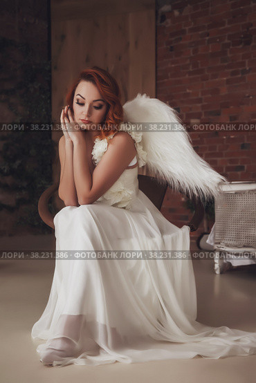 Pretty slender woman with wings. Female in stage image of an angel. Emotion girl in dress sitting on chair in an old textured room. Actress shows abilities. Concept of theatrical premiere. Copy space. Стоковое фото, фотограф Aleksandr Golubev / Фотобанк Лори