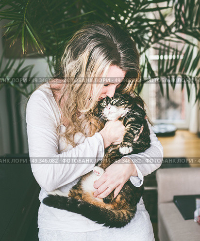 Pretty women in living room holds cat in her arms and cuddle. Стоковое фото, агентство Ingram Publishing / Фотобанк Лори