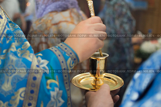 Priest in blue church vestment anoints with sacred oil from golden vessel. Стоковое фото, фотограф irisff / Фотобанк Лори