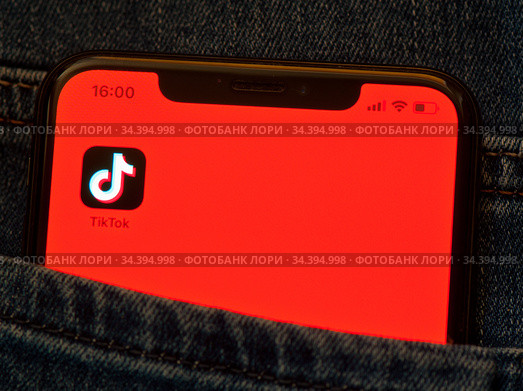 Приложение TikTok ("ТикТок") на экране мобильного телефона, лежащего в кармане джинсов (крупным планом) (2020 год). Редакционное фото, фотограф E. O. / Фотобанк Лори