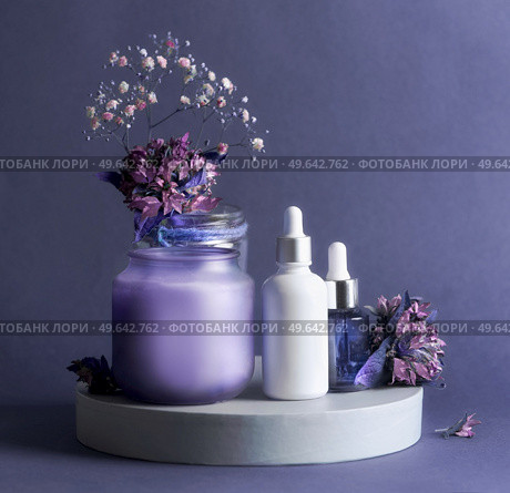 Purple beauty product setting with cosmetic serum bottles, candle and flowers. Healthy skin care products for facial treatment. Front view with copy space. Стоковое фото, агентство Ingram Publishing / Фотобанк Лори