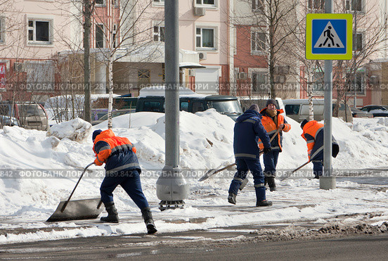 Рабочие гастарбайтеры весной в солнечный ясный день лопатами убирают старый снег с улиц Москвы (2018 год). Редакционное фото, фотограф Наталья Николаева / Фотобанк Лори