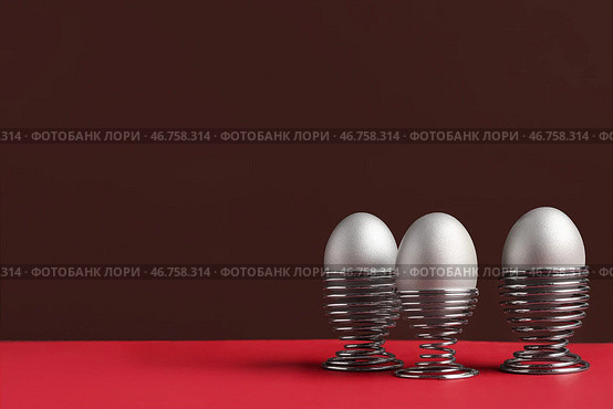 Разукрашенные яйца в подставках на красном столе на фоне коричневой стены. Стоковое фото, фотограф Pixel_shot / Фотобанк Лори
