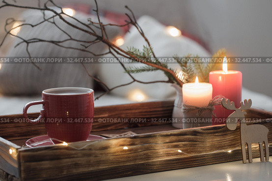 Red cup of tea on tray with burning candles on background sofa with pillows. Cozy home concept. Стоковое фото, фотограф Майя Крученкова / Фотобанк Лори