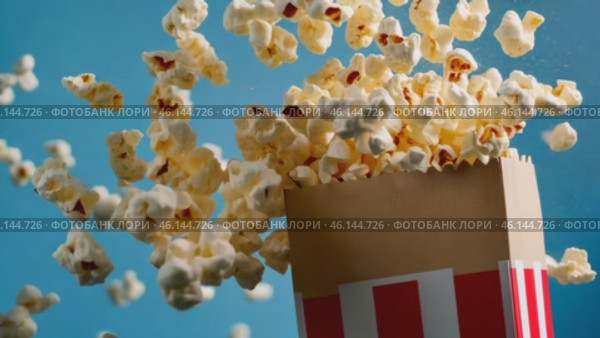 Red white stripe box of popcorn. Popcorn floating out of the paper box, isolated on a light blue background. Striped retro bucket with freshly popped popcorn with some pieces flying. Snack food. Стоковое AI-видео, аниматор Марина Демидюк / Фотобанк Лори