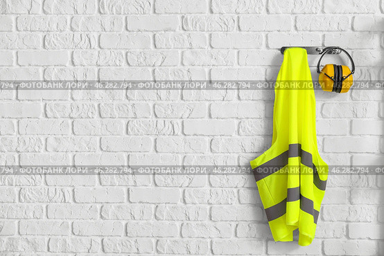 Reflective vest and hearing protectors on white brick wall. Стоковое фото, фотограф Pixel_shot / Фотобанк Лори